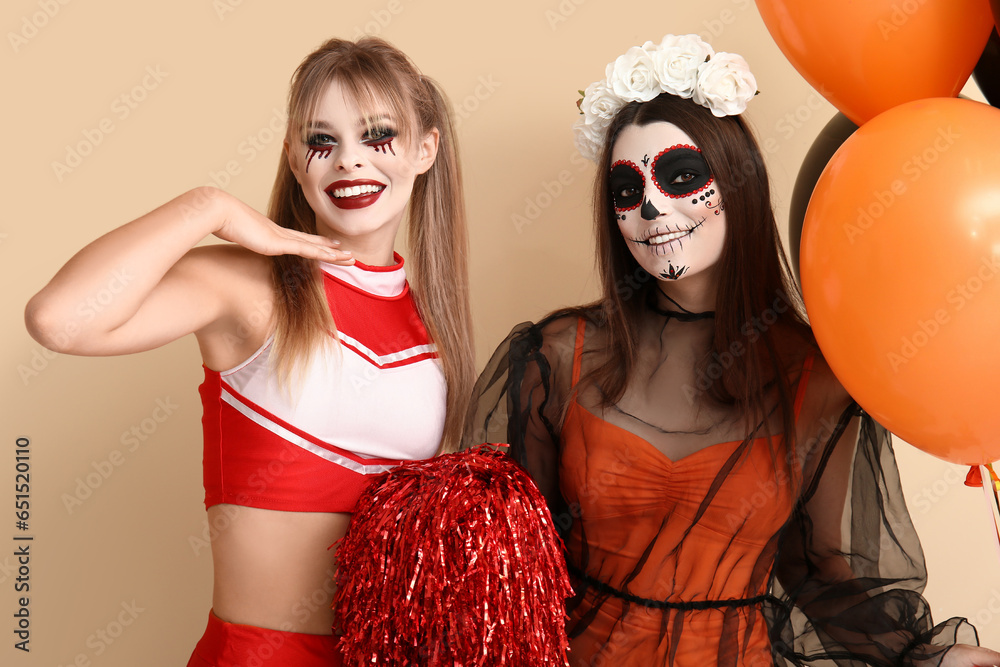 Female friends dressed for Halloween with balloons on beige background