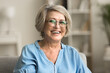 © fizkes - Happy positive blonde elder woman in stylish eyeglasses looking at camera with perfect toothy smile, laughing, posing for home portrait. Beautiful mature lady video call screen head shot