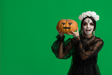 Wall Mural - Beautiful young woman dressed as dead bride for Halloween party with pumpkin on green background