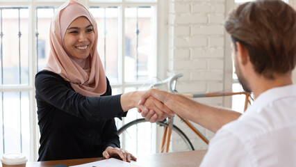 Sticker - Seated at office desk smiling middle eastern ethnicity businesswoman shakes hand european businessman greeting each other starting business meeting, makes offer financial deal, express appreciation