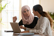 © fizkes - Mixed-race and middle eastern ethnicity women colleagues or students study working together seated at desk in modern office or classroom. Teamwork, cooperation, realization of common project concept