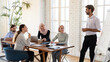 © fizkes - Company owner makes presentation on flip chart for multicultural investors. Diverse workers taking part at seminar educational training led by confident man coach at boardroom, corporate study concept