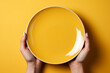 Close-up top view of hands holding empty yellow plate upon yellow table