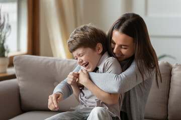 happy young mother and little son having fun on cozy couch in living room, overjoyed mum and prescho