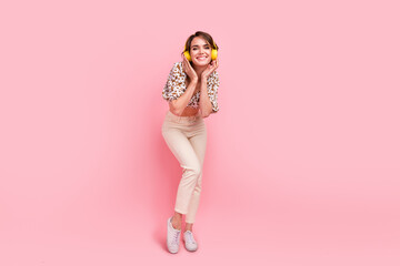 Poster - Full length photo of good mood lovely woman wear print top white pants touching headphones listen music isolated on pink color background