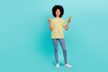 Poster - Photo of funny black skin afro girl wear stylish outfit chevelure advises modern technology shop isolated on cyan color background