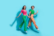 Full length cadre of two sportive glamour wearing clothes girlfriends hands together funky motion isolated on blue color background