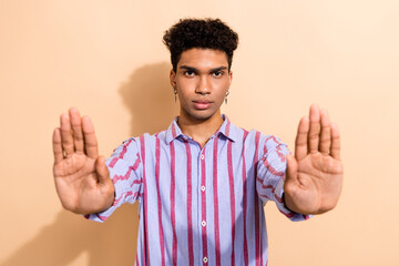 Poster - Portrait of serious confident guy with earrings dressed stylish shirt stretching arms stopping you isolated on beige color background