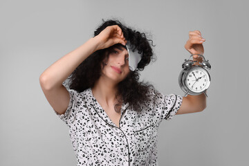 Wall Mural - Tired young woman with sleep mask and alarm clock on light grey background. Insomnia problem