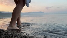 Cold Water Lake Turin On The Border Of Macedonia And Albania, A Teenage Girl Enters The Water, Unrecognizable People Wrapped In A Blanket Over Pebbles At Dawn, Only Legs And Clear Clear Water