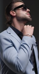 Canvas Print - project video of stylish young man with sunglasses touching beard, looking to side, arranging suit and crossing arms and posing on grey background