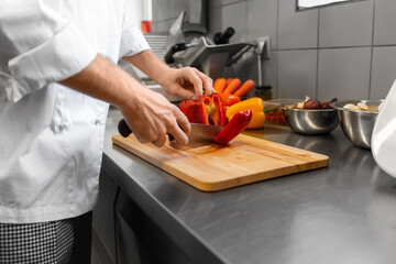 cooking food, profession and people concept - close up of male chef with knife chopping bell pepper on cutting board at restaurant kitchen