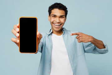 Wall Mural - Young fun man of African American ethnicity he wear shirt casual clothes hold in hand use point finger on mobile cell phone with blank screen area isolated on plain pastel light blue cyan background.