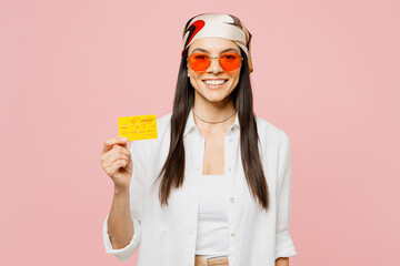 Young smiling hapy fun latin woman she wearing white shirt casual clothes sunglasses hold in hand mock up of credit bank card isolated on plain pastel light pink background studio. Lifestyle concept.