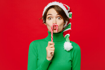 Wall Mural - Young smiling cool fun woman wearing green turtleneck Santa hat posing hold in hand candy cane pov mustache isolated on plain red background. Happy New Year 2024 celebration Christmas holiday concept.