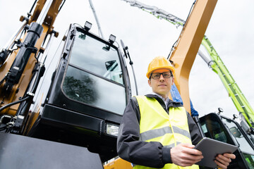 Aufkleber - Engineer in a helmet with a digital tablet stands next to construction excavators.