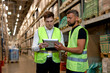© alfa27 - Retail Warehouse full of Shelves with Goods in Boxes, Male Workers Supervisors Holding Paper Tablet Discuss Product Delivery, Dressed in Green Uniform. Distribution Logistics Center