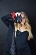 Female model wearing black outfit with black background. Woman holding vintage camera. Charming young woman with blonde hairs and blue eyes.
