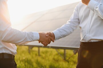 Workers shaking hands on a background of solar panels on solar power plant.