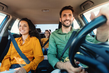 young european parents and daughter riding new car and smiling, enjoying road trip together