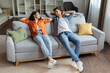© Home-stock - Relaxed indian spouses resting with hands behind head, leaning on sofa, enjoying weekend on comfortable couch in living room at home, full length