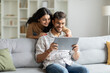 © Home-stock - Happy indian man and woman sitting on couch, hugging and using digital tablet, looking at pad screen and smiling, using newest gadget at home interior