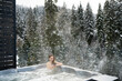 © Daryna  - A young woman looks at the phone while relaxing in a hot tub against the background of Christmas trees in winter. The concept of recovery in a thermal spa