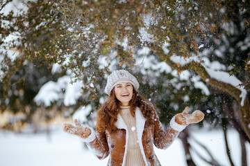 smiling stylish woman in brown hat and scarf catching snow