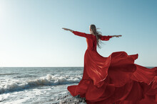 Beautiful Woman In Red Fluttering Dress In The Wind Against The Background Of The Sea
