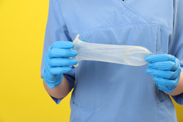 Wall Mural - Doctor with unrolled female condom on yellow background, closeup. Safe sex