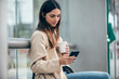 © Westend61 - Young woman with coffee cup using smart phone