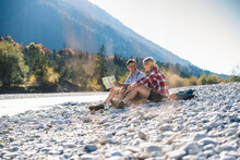 Austria, Alps, Couple On A Hiking Trip Having A Break At A Brook Reading Map