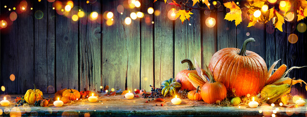 Wall Mural - thanksgiving - pumpkins and corncobs on rustic table with garland and defocused abstract lights