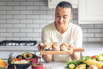 Wall Mural - A young woman with spring rolls in rice paper in the kitchen.