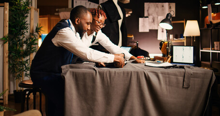 Wall Mural - Two couturiers cutting material for modern clothing items in workshop, using scissors on fabric for handcrafting atelier process. Team of designers preparing for tailoring and needlework.