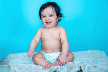 Smiling six months old cute indian baby boy wearing diaper sitting on floor isolated over blue studio background, copy space