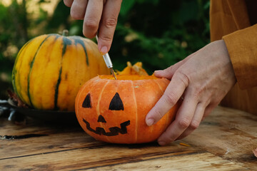 DIY Halloween jack o lantern. Woman carves Halloween pumpkin outside. 