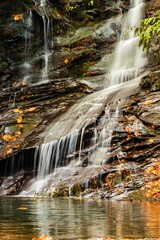 Sticker - Vertical shot of the waterfall water pouring in a lake in the forest on a sunny day