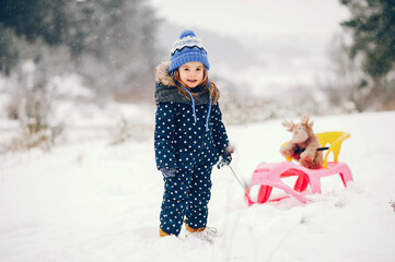 Wall Mural - Little girl in a blue hat playing in a winter forest