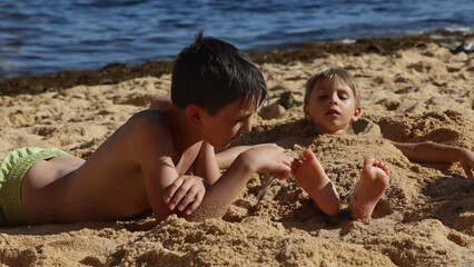 Sticker - Child, tickling sibling on the beach on the feet with feather, kid cover in sand, smiling, laughing, enjoying some fun