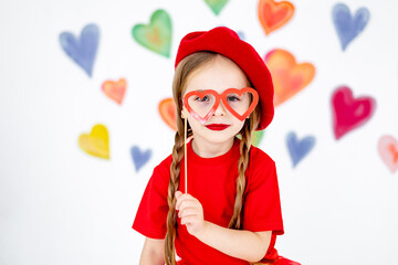 portrait of a little girl in a red beret on a background of hearts with glasses in the form of hearts, a smiling child, a concept for all lovers or Valentine's Day