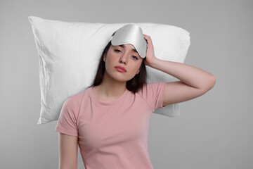 Canvas Print - Tired young woman with sleep mask and pillow on light grey background. Insomnia problem