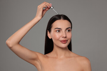 Sticker - Beautiful woman applying hair serum on grey background. Cosmetic product