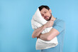 © New Africa - Tired man with pillow on light blue background, space for text. Insomnia problem