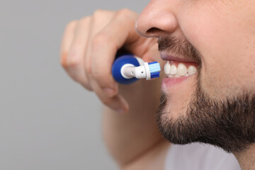 Wall Mural - Man brushing his teeth with electric toothbrush on light grey background, closeup. Space for text