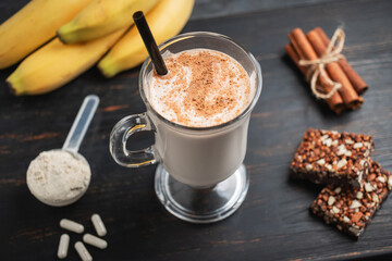 Canvas Print - Glass of protein milkshake drink with straw and scoop of whey protein powder, white capsules of amino acids, vitamins, protein bar and bananas on a dark wooden board, bodybuilding food supplements