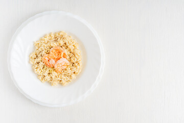 Poster - Top view of homemade creamy italian risotto cuisine made of boiled rice decorated with shrimps or prawns served in plate on white wooden background with copy space for traditional dinner or lunch