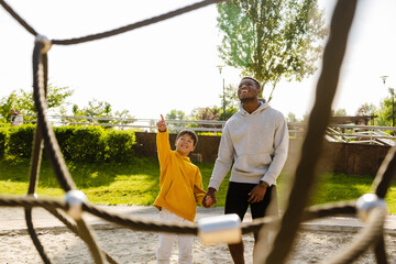 Wall Mural - Smiling african man spending time with his son on playground