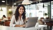 © Serhii - Indian business woman working on a laptop in a bright, open workspace. A young Indian student or remote teacher is working in online education, flexibility of remote work. Generative AI