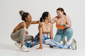 Wall Mural - Group of smiling women in sportswear posing together, doing split over white background